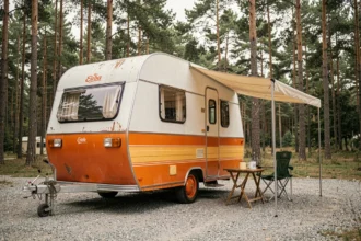Caravane Eriba Puck vintage en occasion stationnée dans un camping sous les pins, modèle culte à carrosserie arrondie blanc et orange