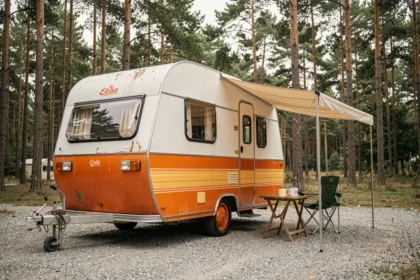 Caravane Eriba Puck vintage en occasion stationnée dans un camping sous les pins, modèle culte à carrosserie arrondie blanc et orange
