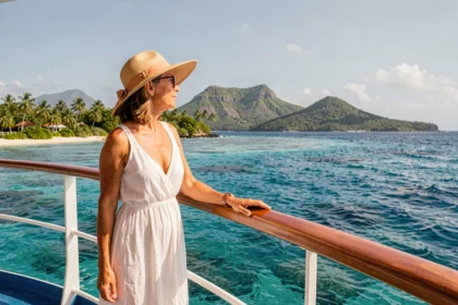 Femme en robe blanche sur le pont d'un bateau de croisière contemplant la côte verdoyante de la Guadeloupe