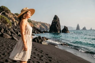 Femme en robe de lin sur une plage de sable noir volcanique des îles Éoliennes avec vue sur la mer turquoise